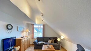 Una sala de estar acogedora con televisión, muebles de madera, un sofá y una ventana con cortinas.