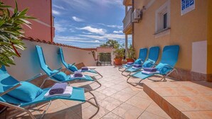 Un espace extérieur ensoleillé, aménagé avec des fauteuils bleus et un sol carrelé.