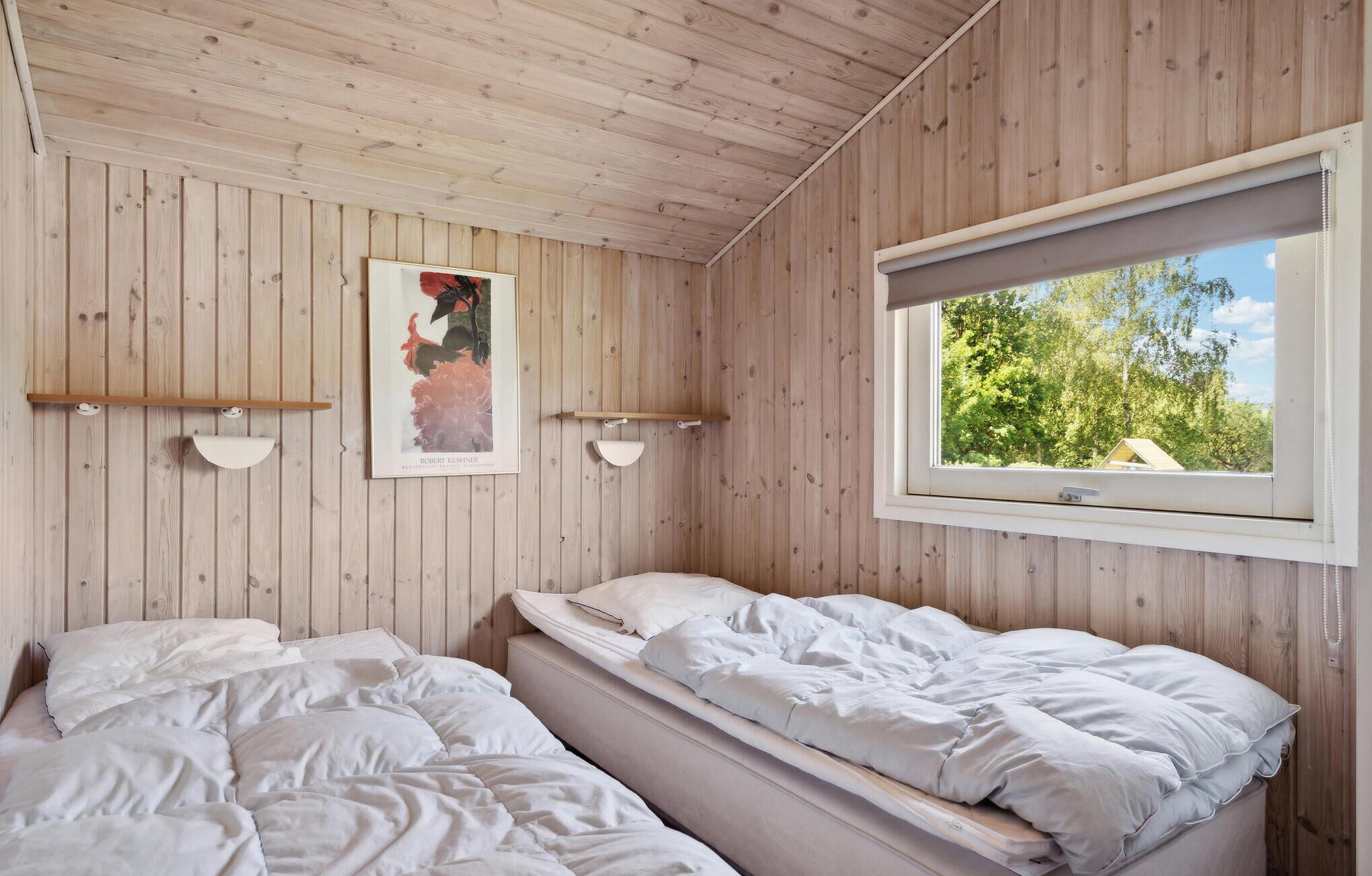 A wooden room with two beds, a window, and a painting on the wall.