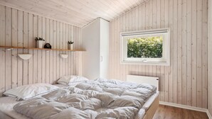 Ein Schlafzimmer mit einem Bett, Holzwänden, einem Fenster mit Blick auf Grünflächen und einem Regal mit Dekoration.