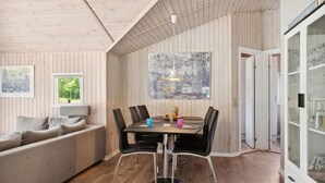 Ein modernes Interieur mit Holzbalkendecke, einer Essecke mit Tisch und Stühlen, einer Couch und einer Vitrine.