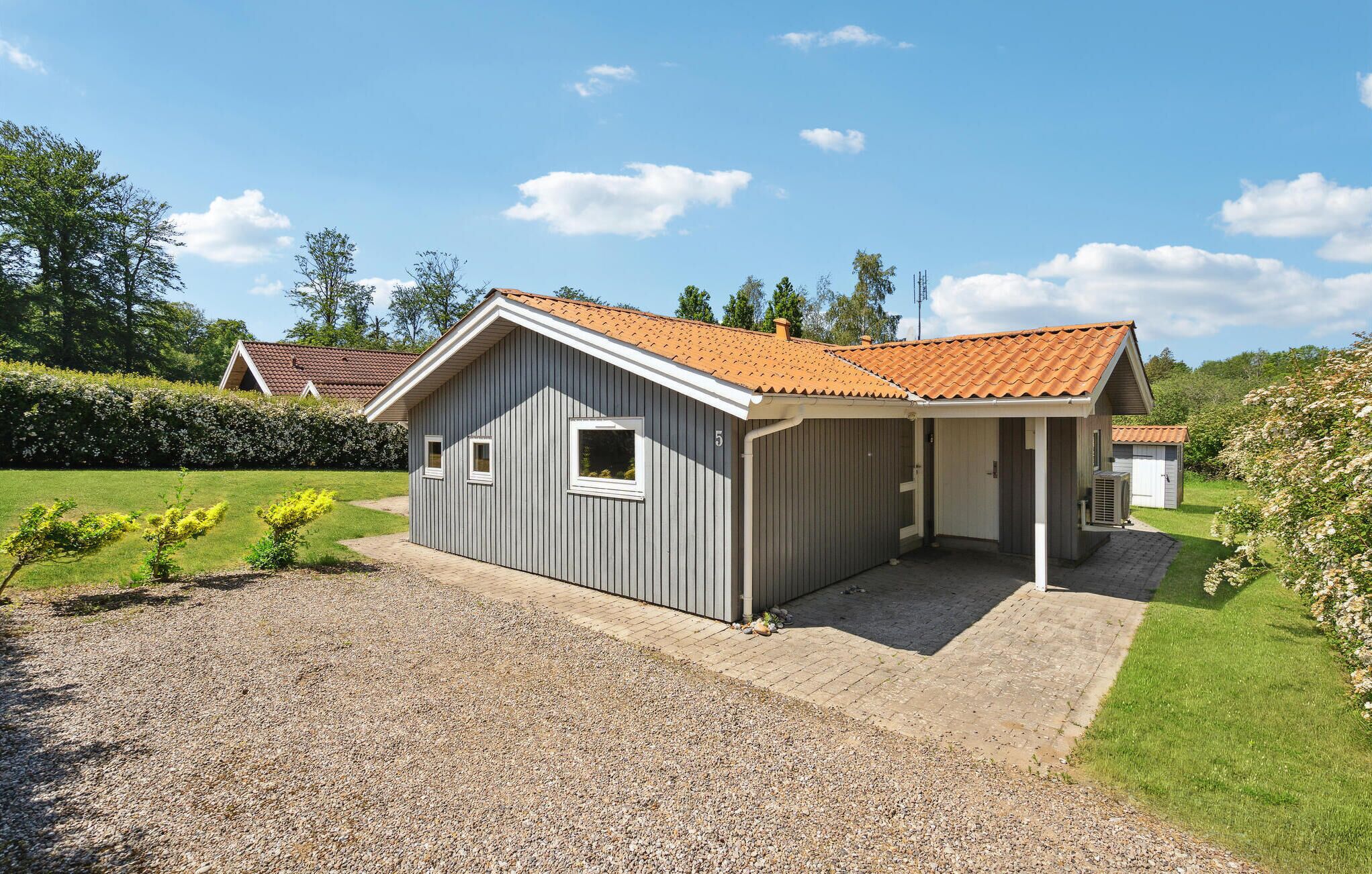 Een gelijkvloers gebouw met een schuin dak, een kleine aangebouwd garage en een grindpad.