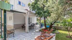 A covered patio area with outdoor seating, a tree, and a view of a building with windows. - Gorgeous home in Jadranovo (Jadranovo)