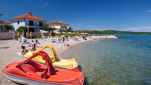 Ein Strand mit klarem Wasser, eine Reihe von Liegestühlen und ein rotes und gelbes Jetski.