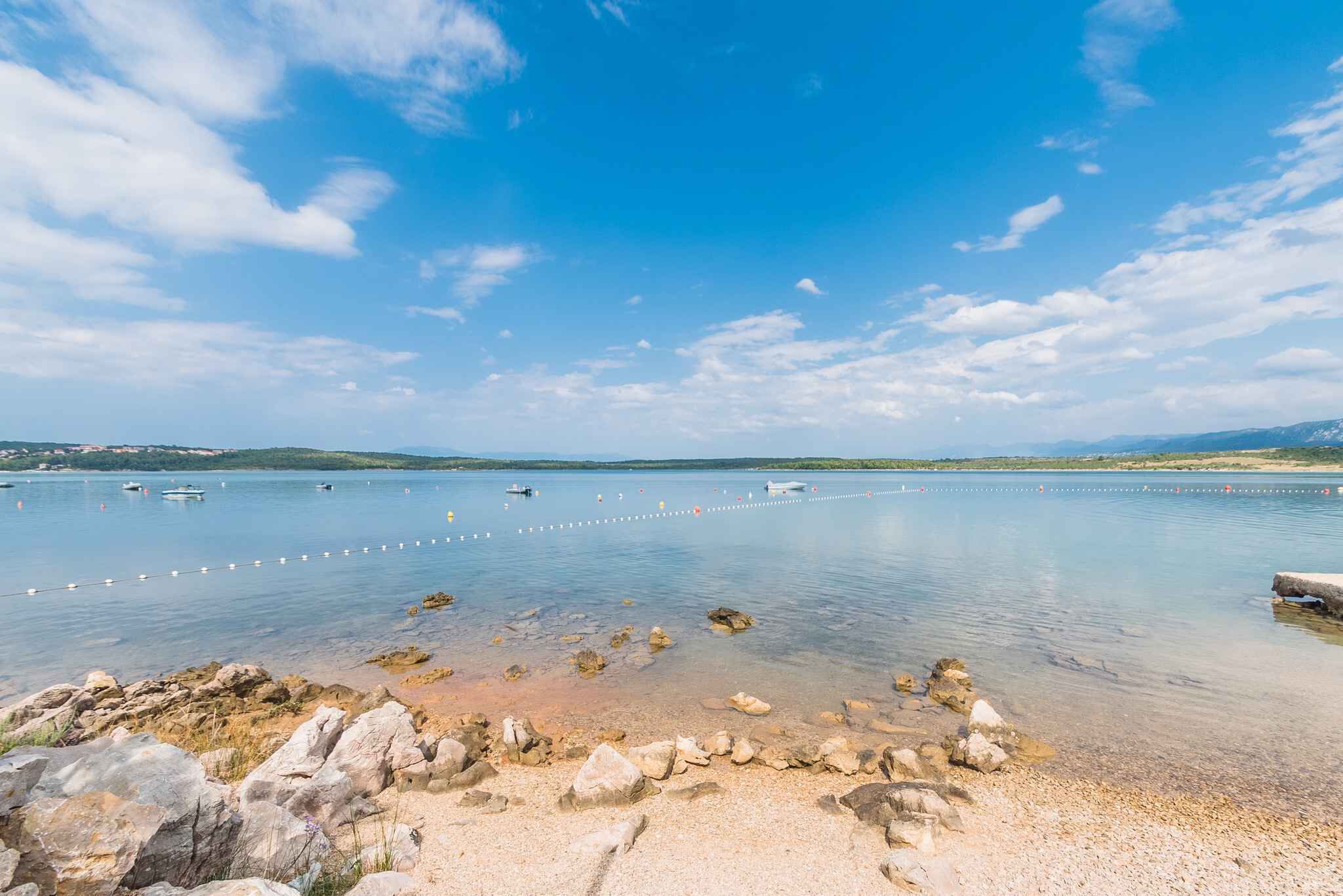 A calm lake with clear water, surrounded by rocks and pebbles.