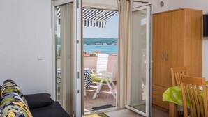 Ein Zimmer mit einer Schiebetür zu einem Balkon mit Meerblick. Ein Holzschrank und ein Fernseher an der Wand sind vorhanden.