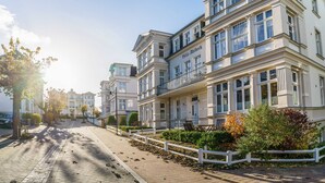 Ein mehrstöckiges Gebäude mit einem Balkon, einer gepflasterten Straße und einem weißen Zaun.