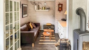 A cozy living room with a sofa, a small wooden table, a fireplace, and a cabinet with glass doors. - Awesome home in Hebnes with house sea view (Hebnes)