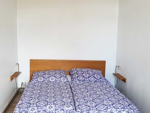 Yhden hengen sänky, jossa on kuviollinen päiväpeite, puinen pääty ja kaksi yöpöytää, joissa on seinään kiinnitetyt lamput.