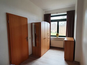 Una habitación con un armario de madera, un radiador, una ventana con cortinas y un jarrón en el alféizar.