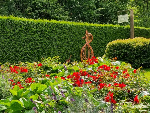 A garden with a variety of flowers, a metal sculpture, and a neatly trimmed hedge.