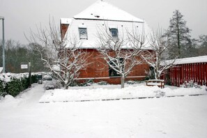 Ein schneebedecktes Gebäude mit Ziegel-Fassade, rotem Dach und einer verschneiten Rasenfläche.