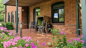 A brick building with a covered patio, outdoor seating, and flowering plants. - Vacation apartment 2 - House Alt Ventschow (Ventschow)