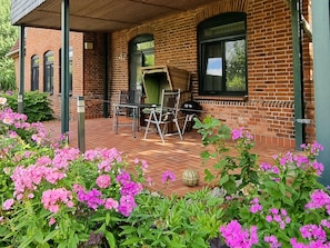 A brick building with a covered patio, outdoor seating, and flowering plants.