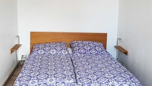 A single bed with a patterned bedspread, a wooden headboard, and two bedside tables with wall-mounted lamps. - Vacation apartment 2 - House Alt Ventschow (Ventschow)