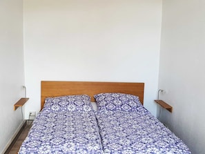 A single bed with a patterned bedspread, a wooden headboard, and two bedside tables with wall-mounted lamps.