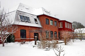 Ein rotbacksteiner Gebäude mit verschneitem Dach und einem kleinen Garten davor.
