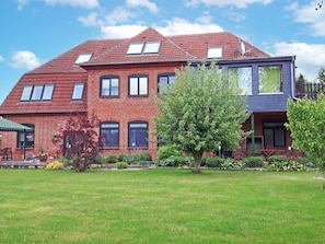 A two-story brick house with a red roof, multiple windows, and a well-maintained lawn.
