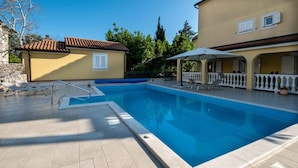 A swimming pool with a tiled deck, lounge chairs, and a covered seating area. - Holiday apartment with shared swimming pool (Malinska)
