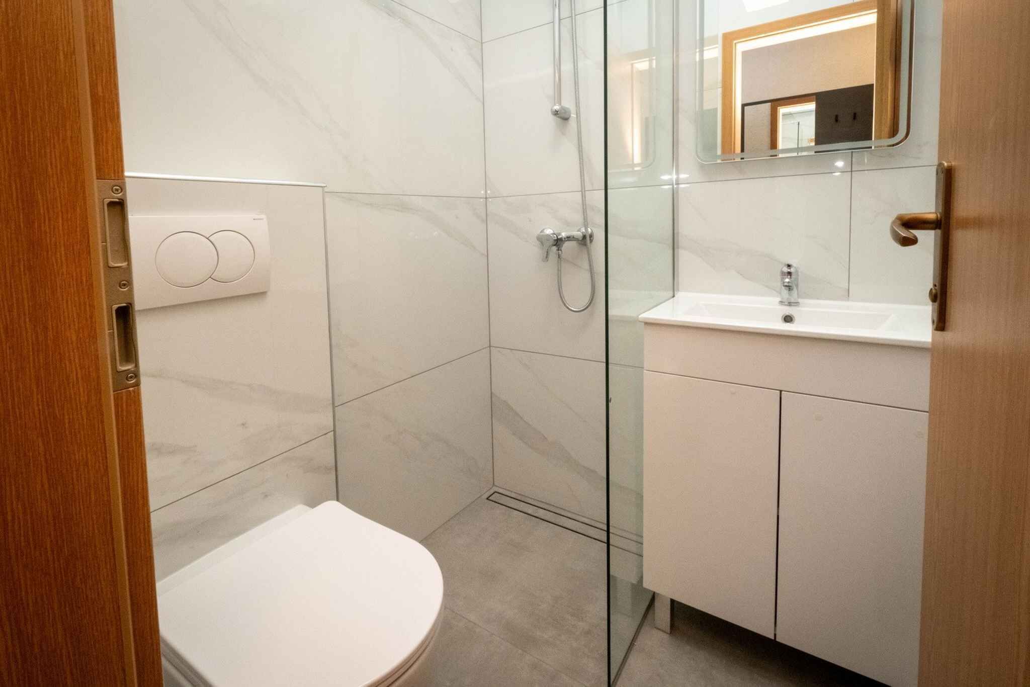 Un baño moderno con cabina de ducha de vidrio, un inodoro blanco y un lavamanos con espejo.