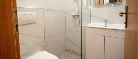 Un baño moderno con cabina de ducha de vidrio, un inodoro blanco y un lavamanos con espejo.