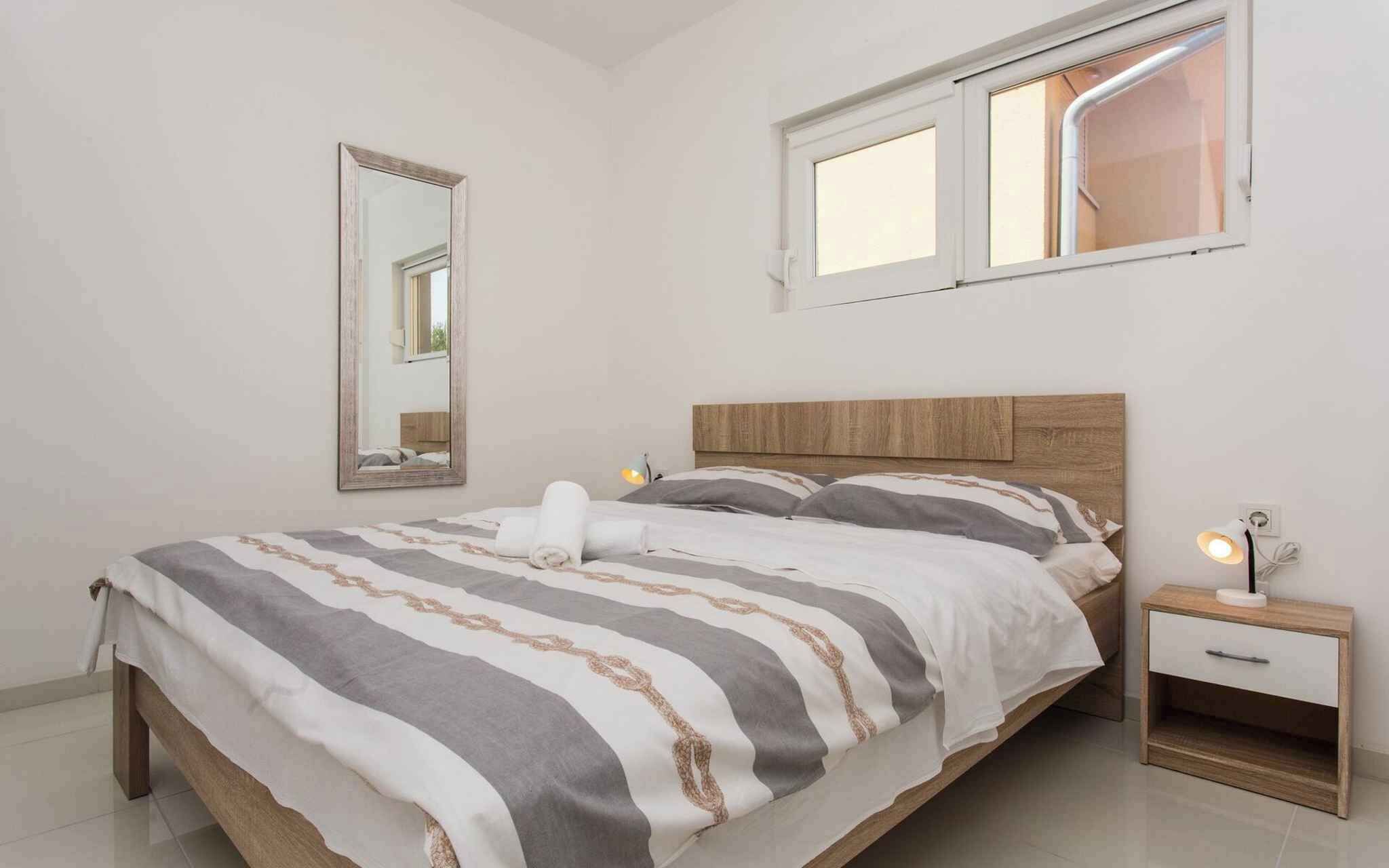 Une chambre à coucher avec un lit, une table de chevet, une lampe, une fenêtre et un miroir.
