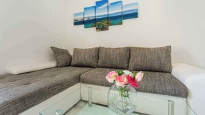 Un salon moderne avec un canapé d’angle, une table basse en verre et un vase rempli de fleurs.