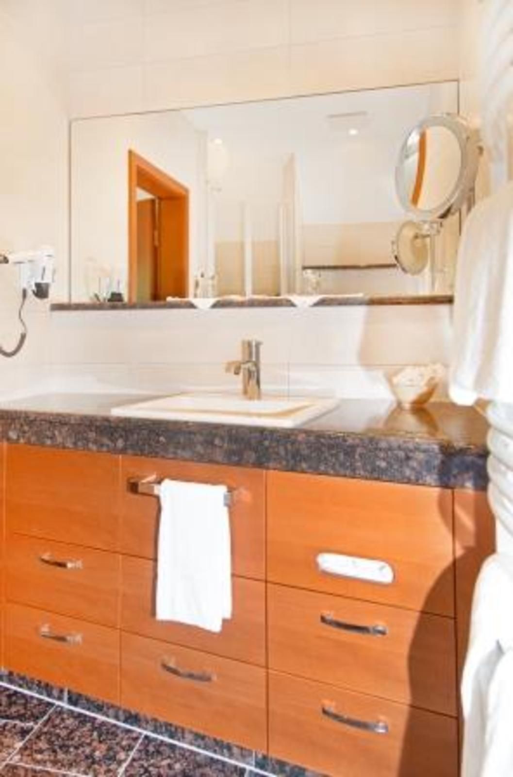 A bathroom with a marble countertop, a sink, a mirror, and wooden cabinets.