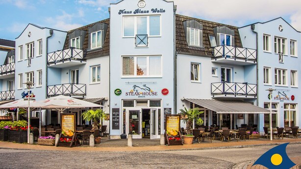 Un immeuble à plusieurs étages, sur lequel on peut lire les inscriptions « Haus Blaue Welle » et « Steak House », indiquant qu’il s’agit d’un restaurant.
