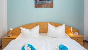 Une chambre d’hôtel avec un lit, deux oreillers, une table de chevet avec une lampe et un tableau représentant une scène de plage.