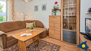 Un salon chaleureux avec un canapé marron, une table basse en bois, une vitrine contenant des objets décoratifs et un téléviseur.