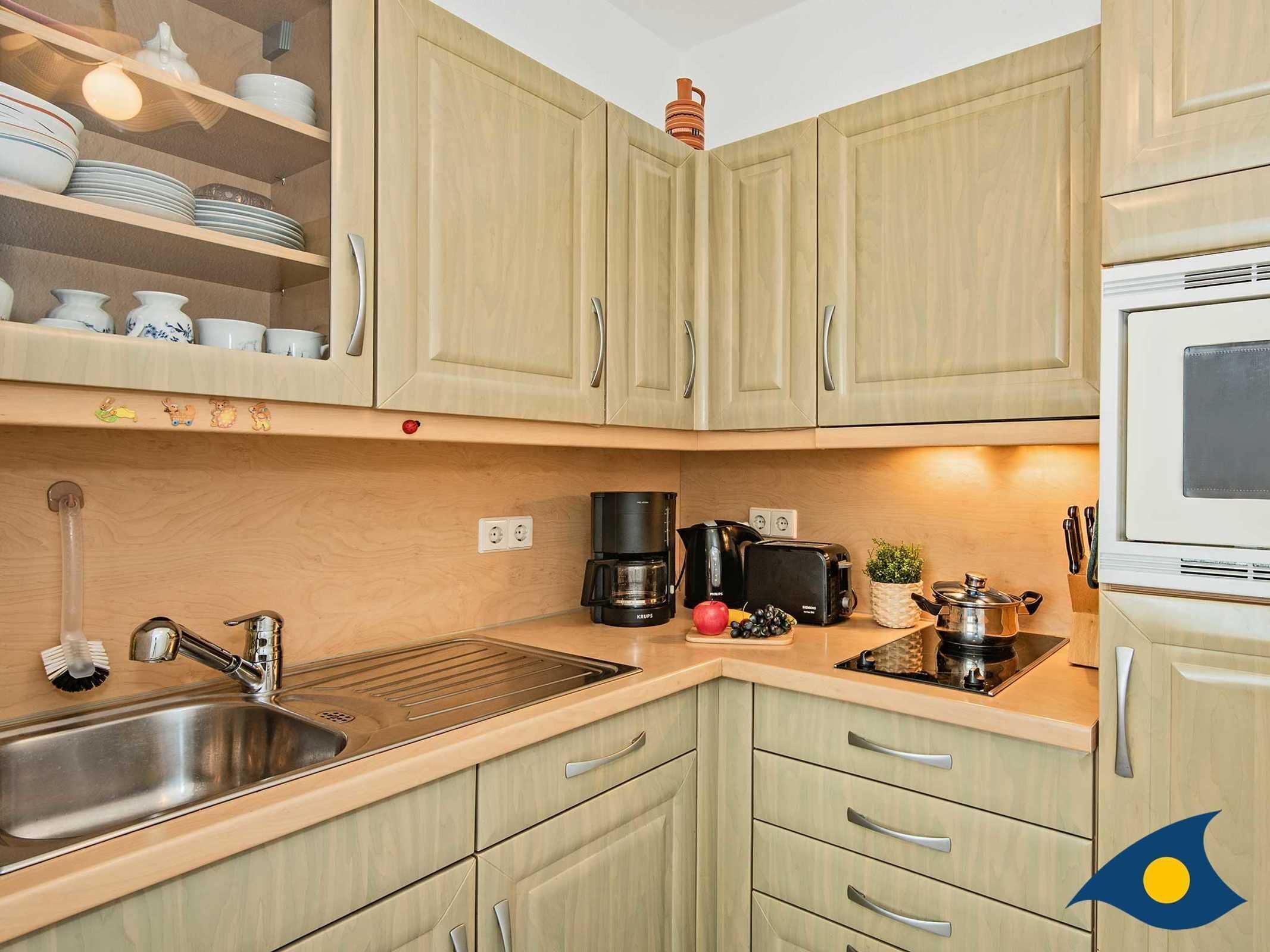 Una cocina con gabinetes de madera clara, un lavamanos de acero inoxidable, una cafetera, un tostador y un microondas.