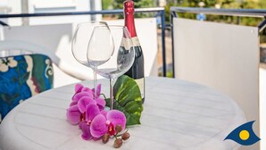 Une table avec une bouteille de vin et un verre sur un balcon donnant sur des immeubles et des arbres.