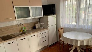 Une cuisine compacte équipée d’un évier, de placards, d’un four à micro-ondes et d’une machine à café. On y trouve une table ronde avec une chaise, ainsi qu’une fenêtre avec des rideaux.