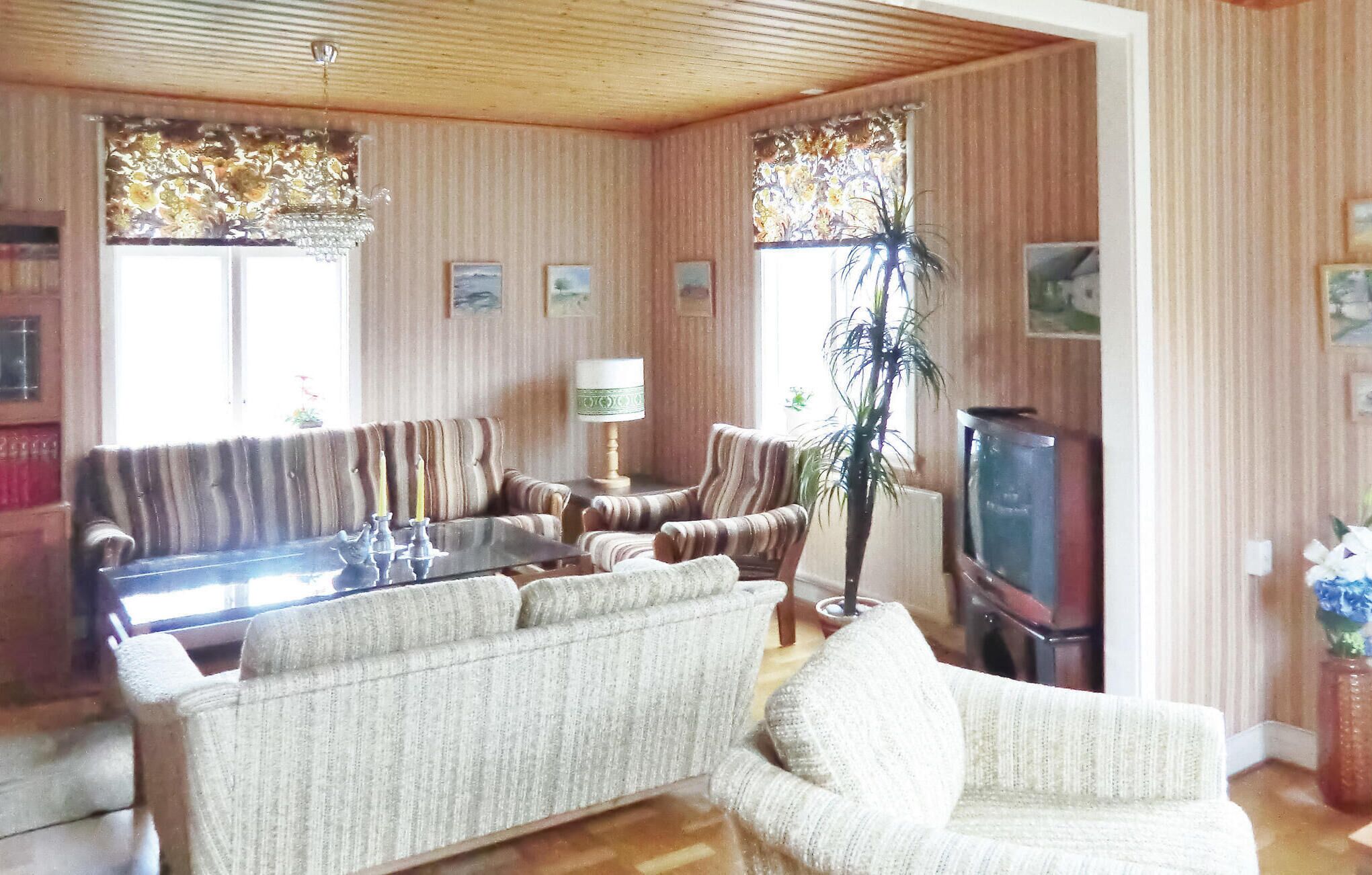 Un salon avec un papier peint à rayures, un canapé, des fauteuils, une table basse en verre, une lampe, un téléviseur et une plante.