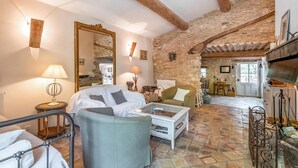 A rustic room with a stone wall, a bed, a sofa, a coffee table, and a dining area with a table and chairs.