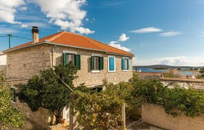 A stone building with a red-tiled roof, green shutters, and a view of a body of water in the background. - Stunning apartment in Drvenik Mali (Drvenik Mali)