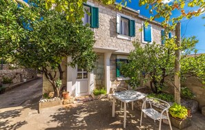 A stone building with green shutters, a small outdoor seating area with a table and chairs, and potted plants. - Stunning apartment in Drvenik Mali (Drvenik Mali)