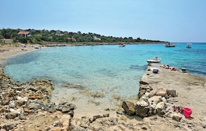 Een kuststrand met helder turquoise water, een rotsachtige kustlijn en boten.