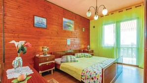 Ein Schlafzimmer mit einer Holzwand, einem Bett mit gepunktetem Überwurf, einem Nachttisch mit Lampe und einem Fenster mit Vorhängen.