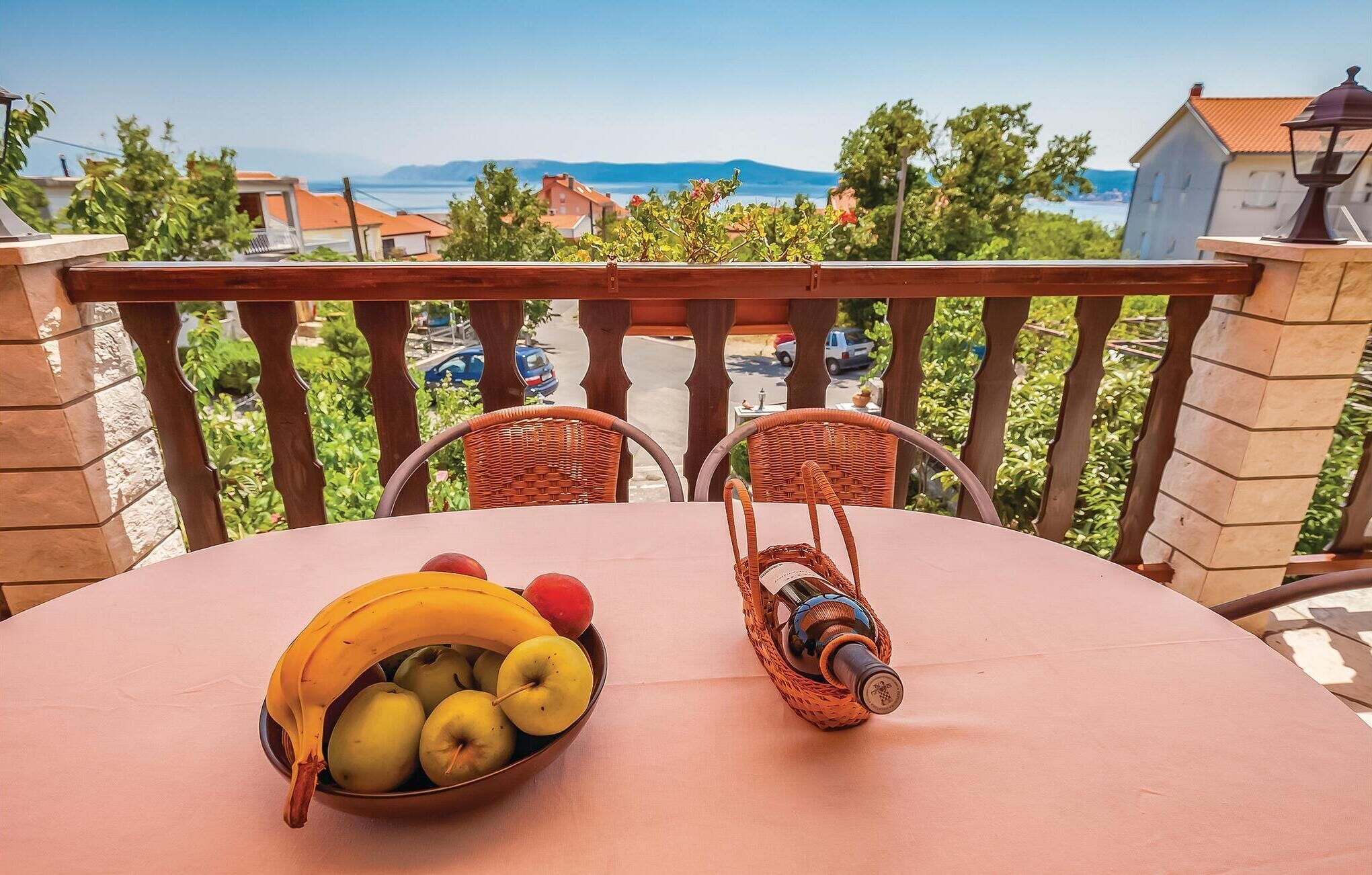 Ein Balkon mit einem Tisch, der für eine Mahlzeit gedeckt ist, mit einer Obstschüssel und einer Flasche.