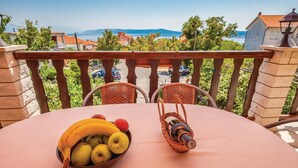 Ein Balkon mit einem Tisch, der für eine Mahlzeit gedeckt ist, mit einer Obstschüssel und einer Flasche.