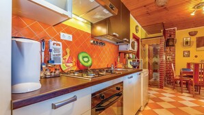 Eine Küche mit Gasherd, Backofen und modernen Geräten. An den Wänden befindet sich Wandkunst mit Obstmotiv, der Boden ist kariert.