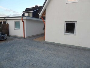 Um edifício residencial com telhado inclinado, uma pequena janela e um pátio pavimentado.