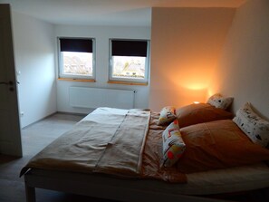 Quarto com cama, duas janelas, radiador e porta.