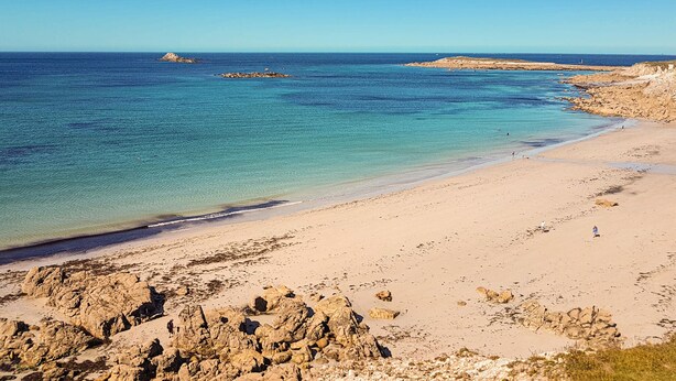 Una spiaggia con acque cristalline turchesi, affioramenti rocciosi e una riva sabbiosa.