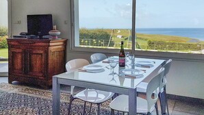Zona pranzo con tavolo apparecchiato per quattro persone, una bottiglia di vino e vista sull'oceano attraverso ampie finestre.