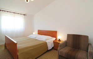 A bedroom with a single bed, a wooden headboard, a nightstand with a lamp, and a brown armchair. - Stunning apartment in Jadrtovac (Jadrtovac)