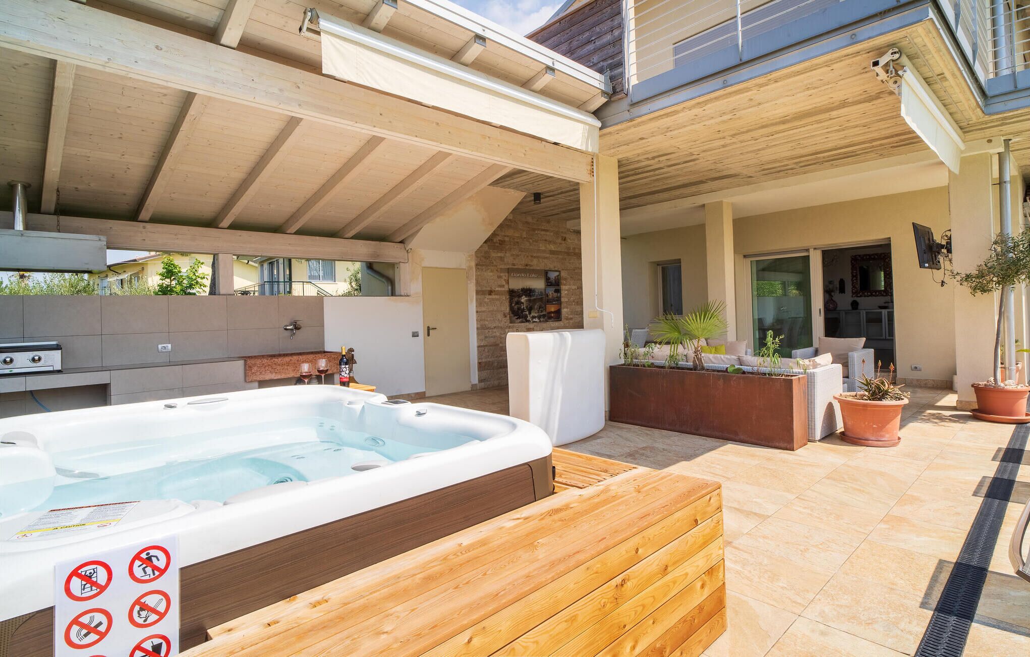 Un espace extérieur aménagé avec un jacuzzi, une terrasse en bois, un barbecue et des plantes en pot.
