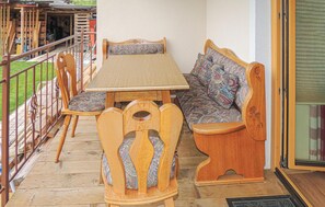 Ein Sitzbereich im Freien mit Holzmöbeln, inklusive Tisch, Stühlen und einer Bank, sowie eine Glastür zu einer überdachten Terrasse.